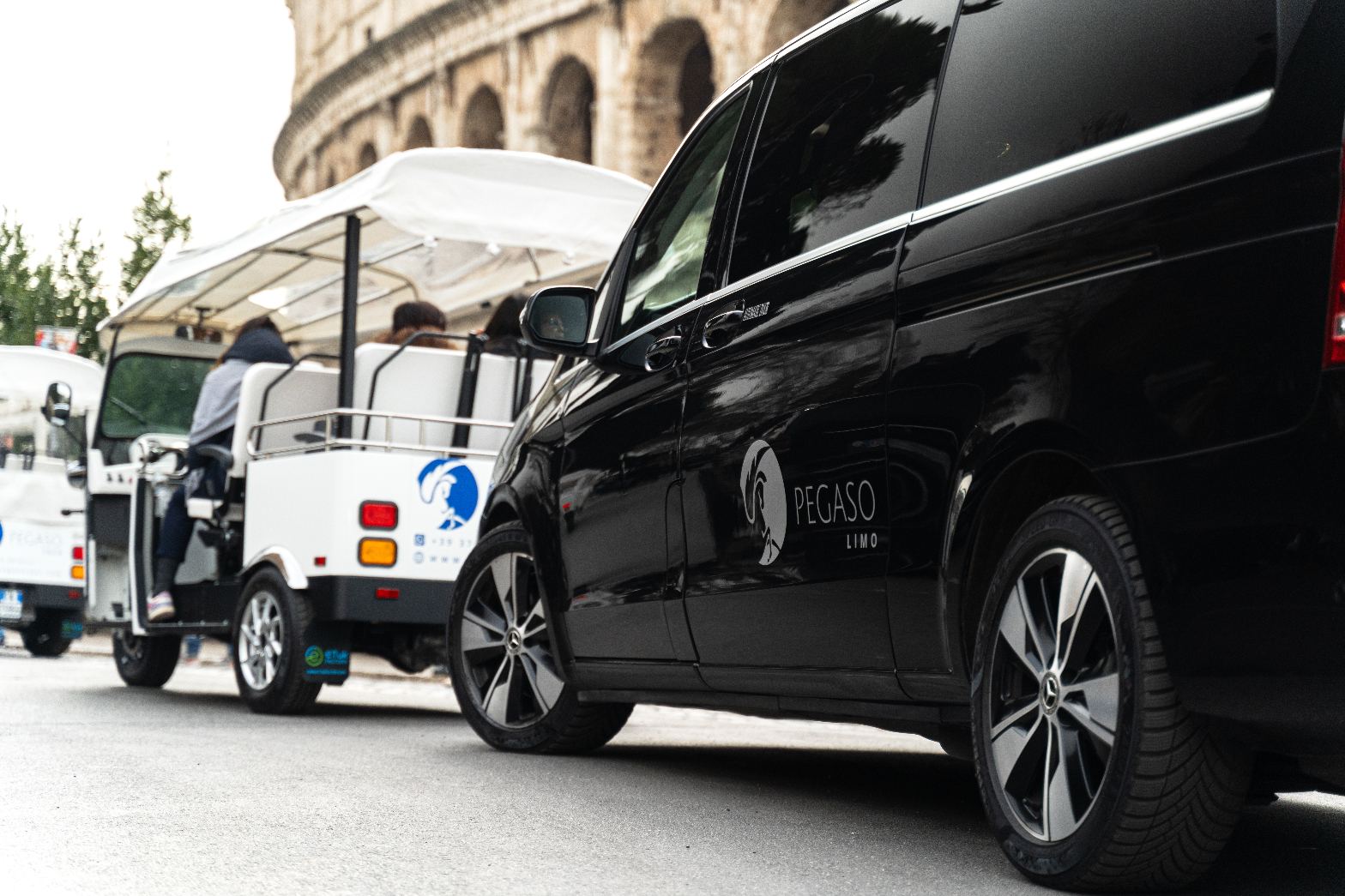 E-tuk tuk bianco e Mercedes nera davanti al Colosseo